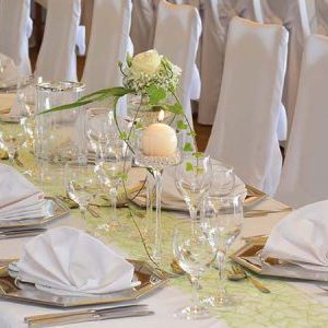 Tischwäsche in Überlänge Elegant gedeckte lange Tafel mit Blumen, Gläsern und dekorativ gefalteten Servietten.